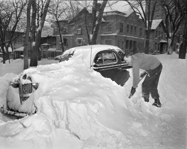Winter scene of Robert Ernst, 207 West Washington Avenue, an airport weather communications employee, trying to shovel his car out of a snow drift.