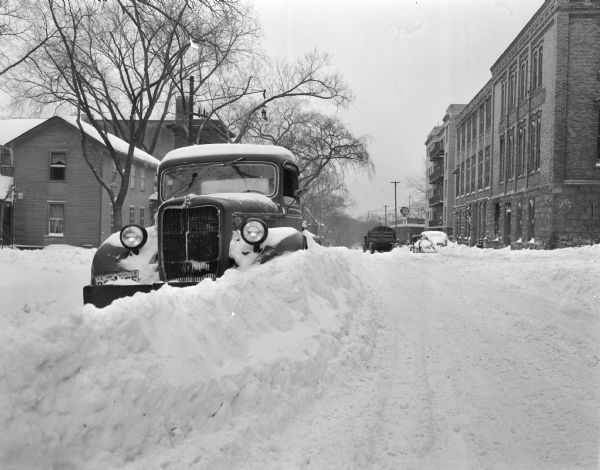 Winter scene looking west along the first block of West Doty Street at a car stuck in a snow bank, Madison, Wisconsin.