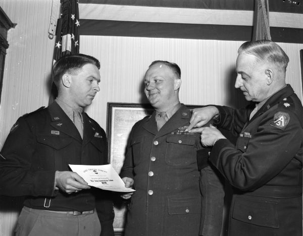 Army recruiter Sgt. Elmer Thompson, Janesville, receiving the Army commendation ribbon from Major Edward Millot, right, field operation officer of the Fifth Army, Wisconsin recruiting district.  Assisting is Captain Vincent S. Dilly (left), commanding officer of the U.S. Army recruiting main station.