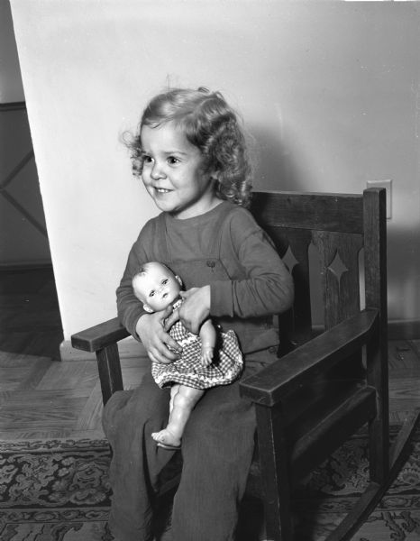 Ann Liddle, three years old, daughter of Prof. and Mrs. Clifford (Ruth) Liddle. She is seated in a rocking chair holding a doll.