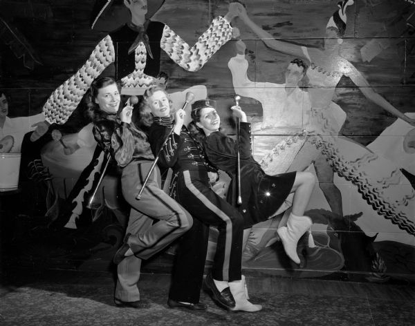 Madison High School drum majorettes posing in their uniforms in front of a mural on a wall. Left to right: Betty Melvin, Central High School; Rebecca Wilson, East High School; and Virginia Kehl, Edgewood High School.