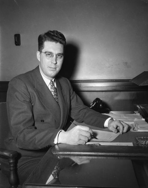 Portrait of J. Rodney Fusch, chairman of Madison's "Brotherhood Week," sitting at his disk in the First National bank, where he is director of personnel.