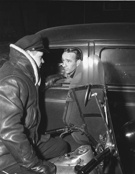 Kenneth H. Sidwell , 17 North First Street, shown talking through the window of his car to Madison police officer Harold Nelson on his motorcycle.  Mr. Sidwell was chosen by the American Automobile Association as the <i>Wisconsin State Journal</i> "courteous driver of the week".