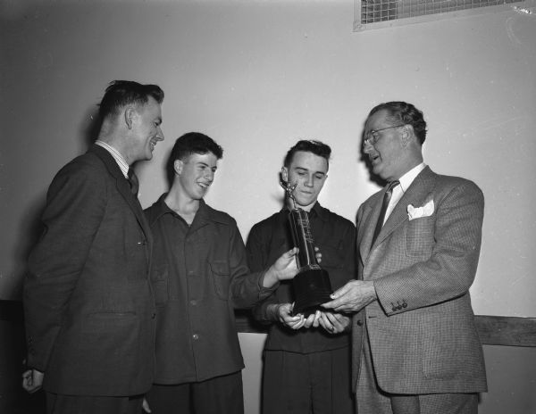 Joseph "Roundy" Coughlin presenting the <i>Wisconsin State Journal</i> Trophy, emblematic of the suburban Six-Man Football league championship, to two members of the Mazomanie football team.  From left to right:  Principal-Coach Stanley Helms; players Tom Zwettler and Richard Nesvacil; and "Roundy".