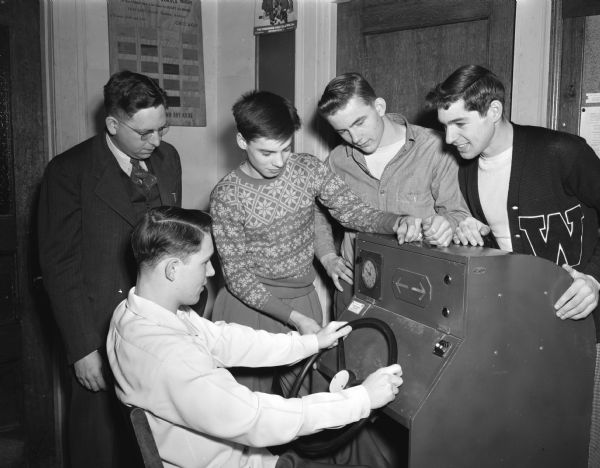 While Ed Tallard takes a reaction test at simulated auto controls in a Wisconsin High School class, his instructor, Homer C. Stahl, (left) and three classmates watch. The other students from left to right are: Pete Conlin, Dick Pigorsch, and Jim Fish.