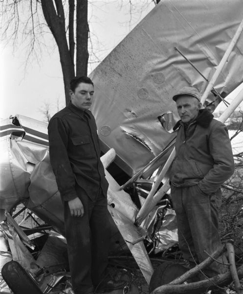 Allen Kielhold (left) and Sam McGaw are shown standing beside the wreckage of the two-seater plane from which they pulled Carl Anderson after he crashed the plane into a road in the town of Fitchburg.