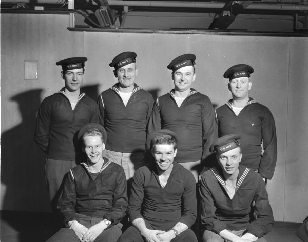Seven Madison men, Naval Reserves, left for New York to ship aboard the USS Wisconsin on a two week training cruise. Left to right seated:  Richard M. Byom, Richard J. Nelson and Milo H. Schimming.  Left to right standing: Gordon J. Bleich, Joseph F. Soehnlein, Lloyd T. Kline and Francis L. Hagan.