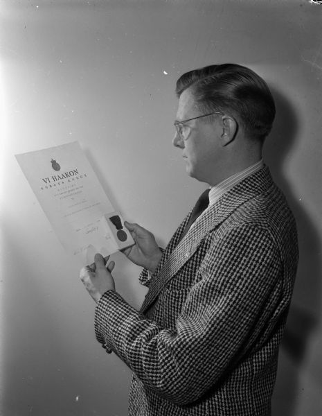 Arnold H. Dammen, assistant director of residence halls at the University of Wisconsin, looking at a letter and a Haakon VII Liberation medal from the King of Norway. Arnold Dammen had worked with the Office of Strategic Services (OSS) during the closing days of World War II, shipping arms and supplies into Nazi-occupied Norway from Sweden.