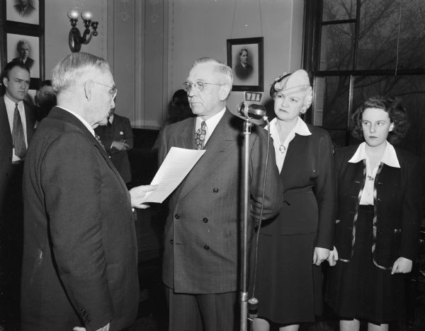 Governor Oscar Rennebohm is administered the oath of office as his wife and daughter look on.
