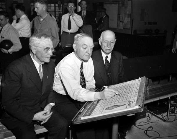 Three justices of the Wisconsin Supreme Court reviewing a score sheet at the Plaza Bowling Alley, 319 North Henry Street. Left to right: Chief Justice Marvin Rosenberry, Associate Justice Elmer E. Barlow and Associate Justice C.A. Fowler.