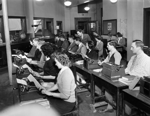 Students seated at typewriters in a classroom with their teacher at the Groves-Barnhart School for Secretaries, 502 State Street.