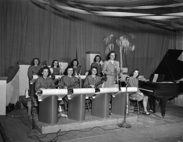 Peggy King, standing with trumpet, and her orchestra, eight women on stage with instruments and music stands.  They played for the Dane County Red Cross dance at the Hotel Loraine on April 12th, 1947.