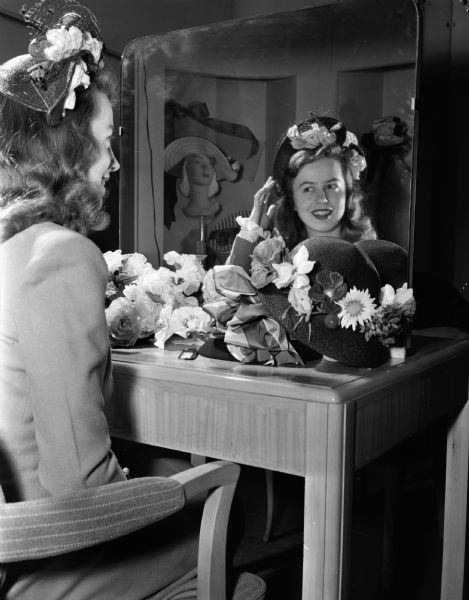 University of Wisconsin Women's Self-Government Association style show  model, Kitty Craig, looks at her image in a mirror as she is modeling a hat chosen at a Madison department store.