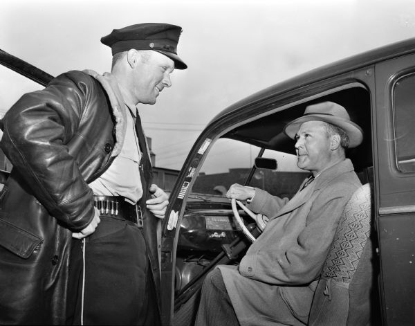 Pictured are Lawrence E. Bowers, seated in his car, and police officer, Robert O'Brien, who is giving Mr. Bowers an award for courteous driving. Mr. Bowers, who lives at the YMCA, is a World War II veteran, having been discharged with the rank of major, and is an accountant for Madison-Kipp Corporation.