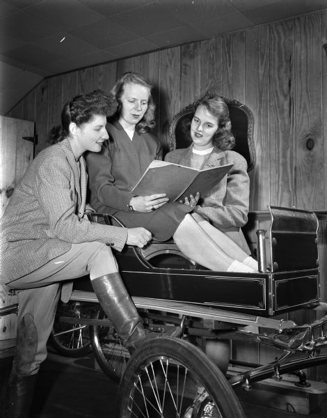 Three committee members of the University of Wisconsin Hoofers' Club making plans for the club's horse show. From the left, posed around a horse-drawn cart, are Marguerita Aylward, Milwaukee, chairman of prizes and awards; Frances Stone, Oak Park, Illinois, and Janet Rausch, River Forest, Illinois. Frances and Janet are co-chairmen of the show committee.
