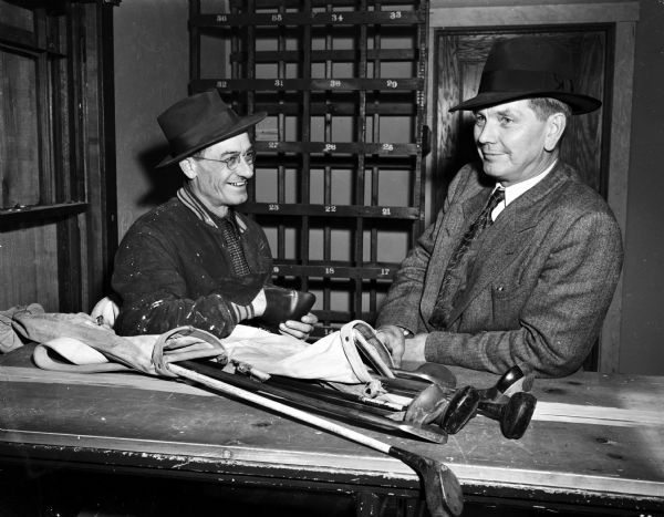 Pictured left to right are Louis Waldorf, manager, and E.C. "Ole" Severson, owner, of the recently remodeled Burr Oaks public golf course on South Park Street. The two men are shown in the office of the club house with a set of golf clubs.