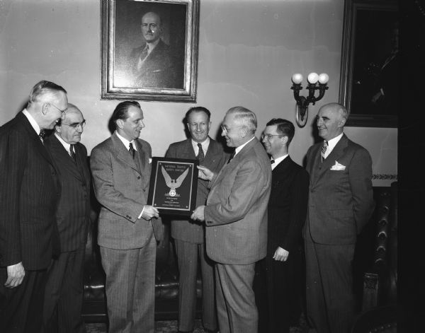 Harry Porter, Jr., representing the National Safety Council, Chicago, presenting a plaque to Governor Rennebohm in recognition of an outstanding state traffic safety record. Also present at the ceremony are, from left, James R. Law, chairman of the state highway commission; Ben L. Marcus, commissioner of the motor vehicle department; Porter; Fred G. Bishop, first assistant state superintendent of public instruction; Governor Rennebohm; Prof. Leonard Hillis, University of Wisconsin, extension division; and R.C. Salisbury, director of the safety division of the motor vehicle department.