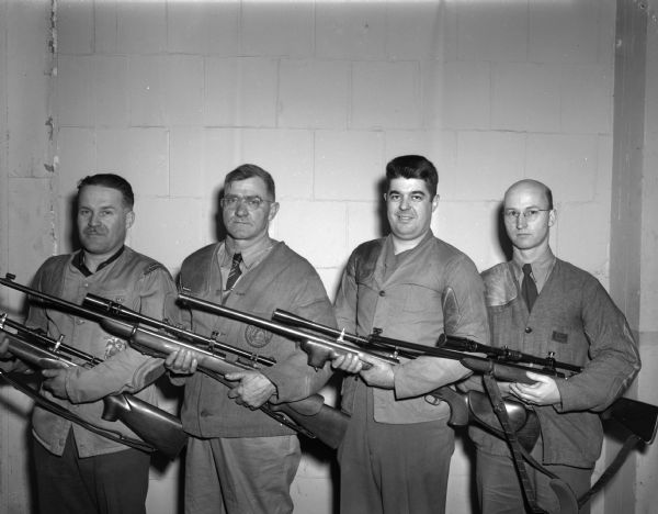 Group portrait of the Madison Rifle Club team holding the Dick Falk trophy they recently won in the Falk Rifle Club's small bore tournament in Milwaukee. Pictured left to right are: Ted Church, Forrest Henderson, Major Ellis Lee, and Jerry [name obliterated.]