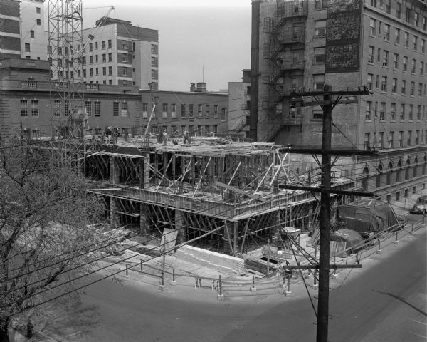 Elevated view of men pouring cement into the forms of the Wisconsin Telephone Company's new seven story building on the corner of West Main Street and South Fairchild Street.