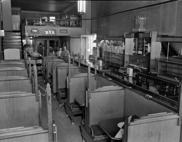 Olympic Restaurant and Bar interior at 125 West Mifflin Street and North Fairchild Street, showing booths and counter, and balcony. A man and woman stand in the background.