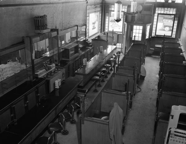 Interior of Olympic Restaurant and Bar, taken from balcony, at 125 West Mifflin Street and North Fairchild Street, showing booths and counter. A man can be partially seen sitting on the floor in front of a booth.
