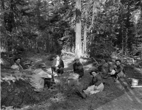 Six men seated in a circle in a wooded area at Island Lake, Ontario, Canada.