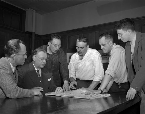 <i>Wisconsin State Journal</i> executives shown in publisher's office, 115 South Carroll Street, reading and discussing a newspaper. Left to right: John Canny, circulation department; (next four unknown); far right, Martin Wolman.