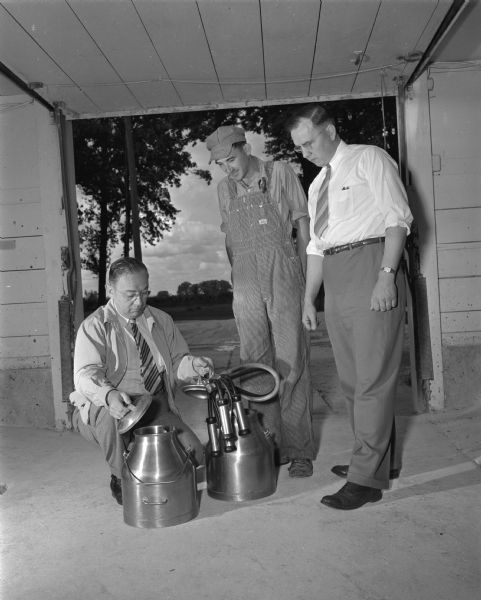 Two men showing a farmer milking equipment.