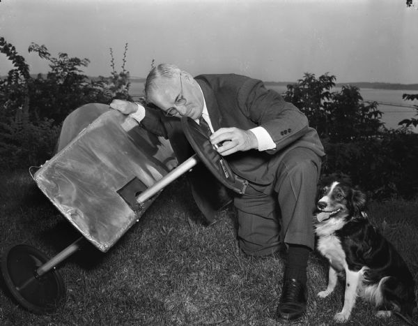 Dane County Judge Fred Evans inspecting Pierre Slightam's racer, the Doodlebug, in his role as chief judge for the Derby. A dog is standing nearby.