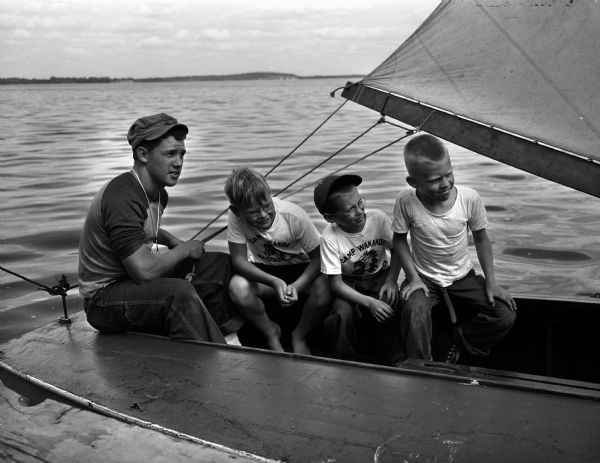Sailing instructor at YMCA Camp Wakanda Harry Stuhldreher Jr. is shown steering a sail boat on Lake Mendota with (L to R) Timothy Rice, Dick Lower, and Randy Conners.