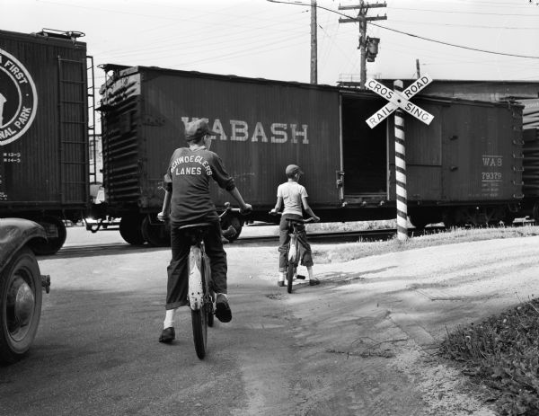 Two children on bicycles waiting for a Milwaukee Road train to "unblock" the entrances to Brittingham Park. Most children not on bicycles crawled under the train.