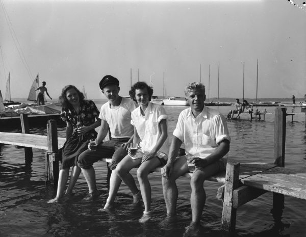 Mendota Yacht Club members, sitting on the pier behind the James Payton house, 409 N. Blair Street. Left to right:  Ann Dre Schlimgen, James Payton, Parnee Bush, and John Sisk.