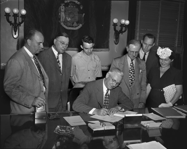 Looking on as Governor Oscar Rennebohm signed the Youth Service Bill were, left to right: Frank C. Ross, Senator Rudolph Schlabach, Tom Peterson, Judge Albert H. Schmidt, Bjarne Romnes, and Mrs. R.L. Schumpert. The Youth Bill aimed at restoring the state's youthful delinquents to useful society through more understanding treatment and better facilities.