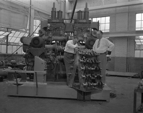 Display of a 50-ton machine, developed by the Gisholt Machine Company, that will help speed up production of automobile crankshafts. W.A. Smlja, on the left, is master mechanic for the Plymouth division of the Chrysler Corp. and Charles H Foster, Gisholt sales manager is on the right.  The machine, first of its kind to be invented, can out six crankshaft pins in a single operation.