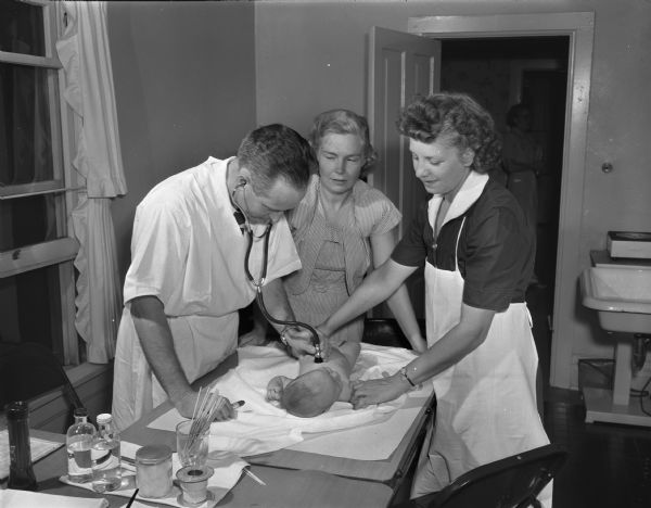 Visiting Nurse Service volunteers, sponsored by Attic Angels, conduct a child health examination at Longfellow School. Rea Ragatz, center, is watching Dr. William Moore and Myrtle Spencer examine one of the babies.