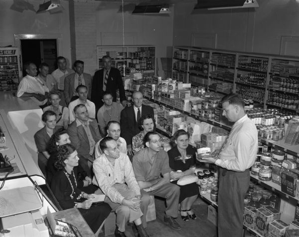 Members of the Madison Labor Co-op committee are shown at a meeting at the new East side co-op grocery store, 3055 East Washington Avenue, which will have its formal opening on October 4, 1947.  Pictured standing in the front of the committee is Gordon Bergenske, chairman, telling the committee about co-op products.  Pictured standing in the back, second from the left, is Ervin Bruner, acting manager, Consumer Co-op Service.