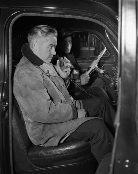 Fire Chief Edward J. Page is broadcasting instructions to an aerial truck using new mobile radio equipment with driver, Fireman Frank McMahon. The mobile radio system was the first fire department system in the state.