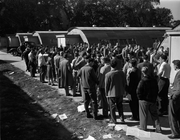 A large group of students in a Veterans' Administration registration line outside a collection of Quonset huts on the campus of the University of Wisconsin-Madison.