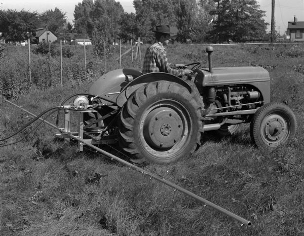 Man on tractor in field using a spray bar that was fabricated by Kupfer Foundry and Iron Works, Inc., 101-149 Waubesa Street.