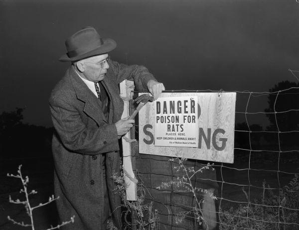 James L. Clarke, city health inspector, placing a warning sign on a fence at the Shorewood dump after workers distributed poison bread bait in the dump.