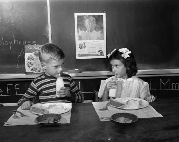 Two school children, a boy and a girl, drinking milk from bottles in their classroom with an American Dairy Association poster in the background. Taken for the American Dairy Association of Wisconsin.