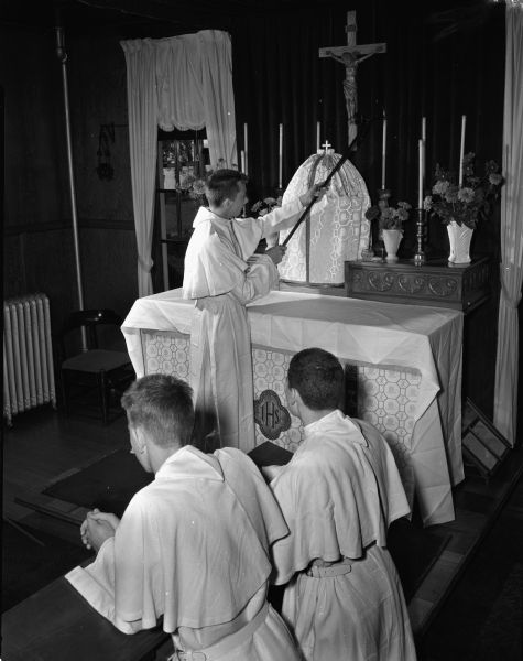 Norbertine Novitiate Chapel, showing Jerome Tremel and Angelo Frascino kneeling in prayer, with John Patrick Shaughnessy lighting the candles at the altar. The chapel was once a ballroom when it was the home of Frank Allis. The Novitiate is at 4123 Monona Drive.