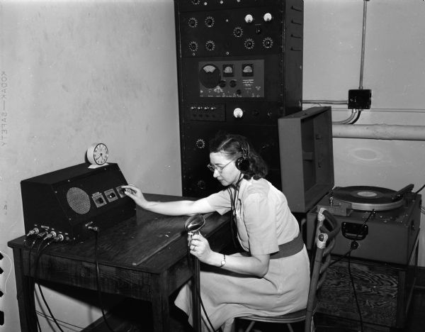 Woman seated at radio broadcasting console playing music for patients at the Veterans Administration Hospital on the grounds of Mendota State Hospital.