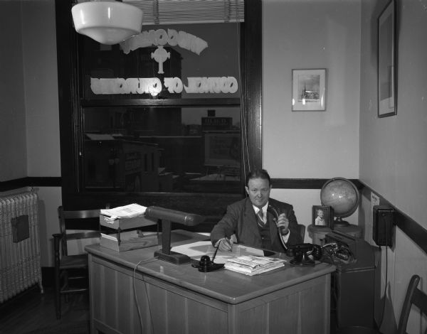 Man (Ellis H. Dana?) seated at desk and dictating into a machine, in Wisconsin Council of Churches office, Room 353, Washington Building, 119 East Washington Avenue.