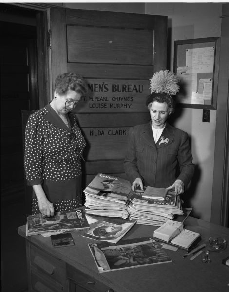 Two women sorting magazines to be distributed to the Veterans' Hospital, Lake View Sanatorium and nursing homes in Madison.  Left to right are Sgt. M. Pearl Guynes, 204 North Pinckney Street, Womens' Bureau, Madison Police Department, and Alice Cummings, 429 West Wilson Street.