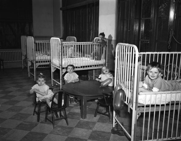 A ward at the Wisconsin Orthopedic Hospital, 1415 Linden Drive, showing three children in cribs, and a small table with three toddlers seated in small chairs.