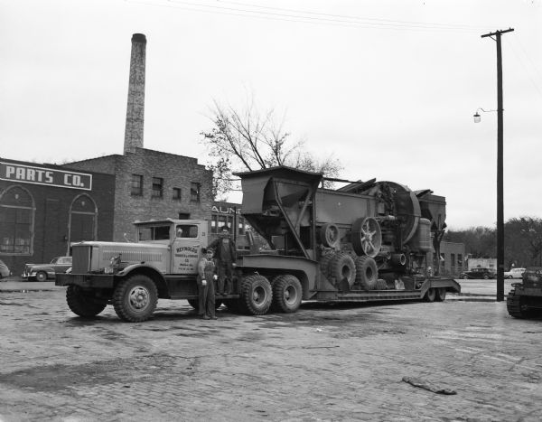 Reynolds Transfer flatbed trailer truck with large load of industrial equipment with two men standing by the cab.