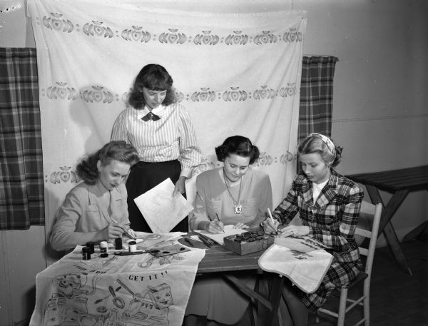 Four members of the University of Wisconsin Dames Club doing textile painting.  Left to right are Mrs. William E. Peterson (standing), chairman of the group, Mrs. Clifford Lardinois, Mrs. Robert F. St. John, and Mrs. Lee Robert White.