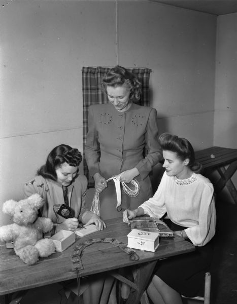 Three members of the University of Wisconsin Dames Club making Christmas gifts.  Left to right are Mrs. Marvin D. Whitehead, Mrs. John S. Boyle (standing), and Mrs. Walter P. Ziarnik.
