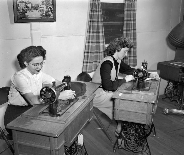 Two members of the University of Wisconsin Dames Club working on sewing projects with the "new look". Treadle sewing machines were used. Mrs. W. James Harper is on the left and Mrs. Paul M. McMinn is on the right.